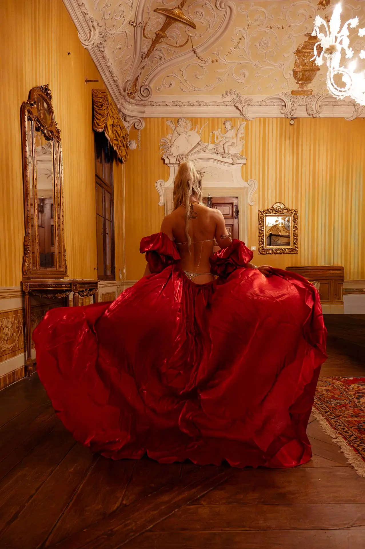 ritratto-ambientato-book-fotografico-performer-brescia-verona Ritratto ambientato per book fotografico performer a Brescia e Verona: modella di spalle in ampio abito rosso scenografico all'interno di una villa storica.